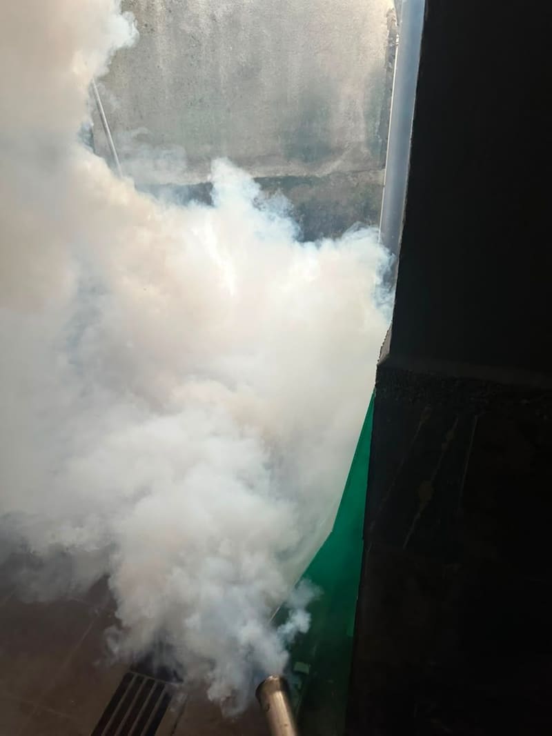 Fogging machine releasing a cloud of insecticide fog along a fence