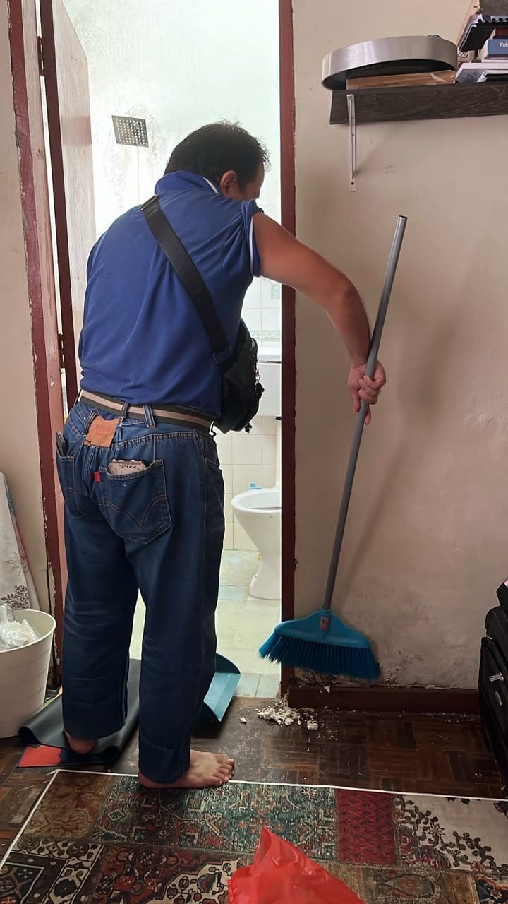 Technician sweeping up soil and debris at the base of a door frame during a termite job
